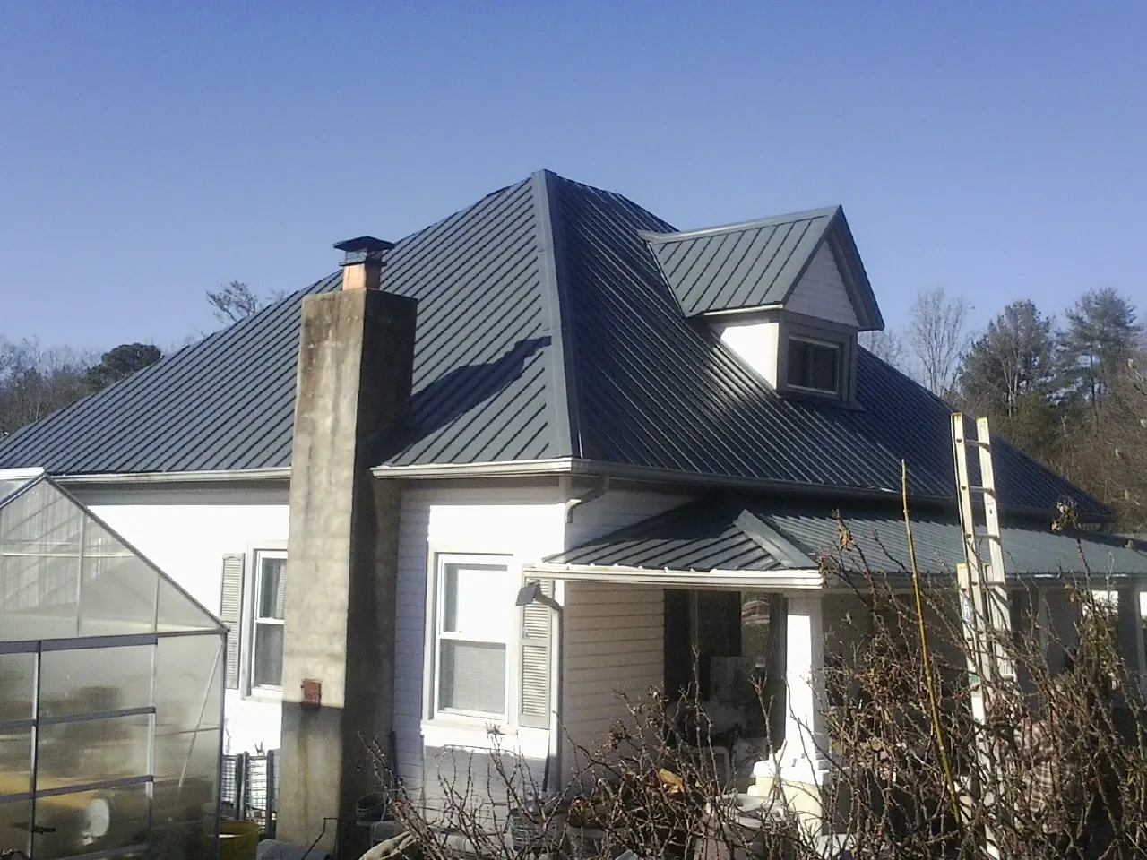 Dark blue standing seam metal roof on a white farmhouse with dormer — Slate & Tile Roof Repair by Roofing Brothers in Aulander