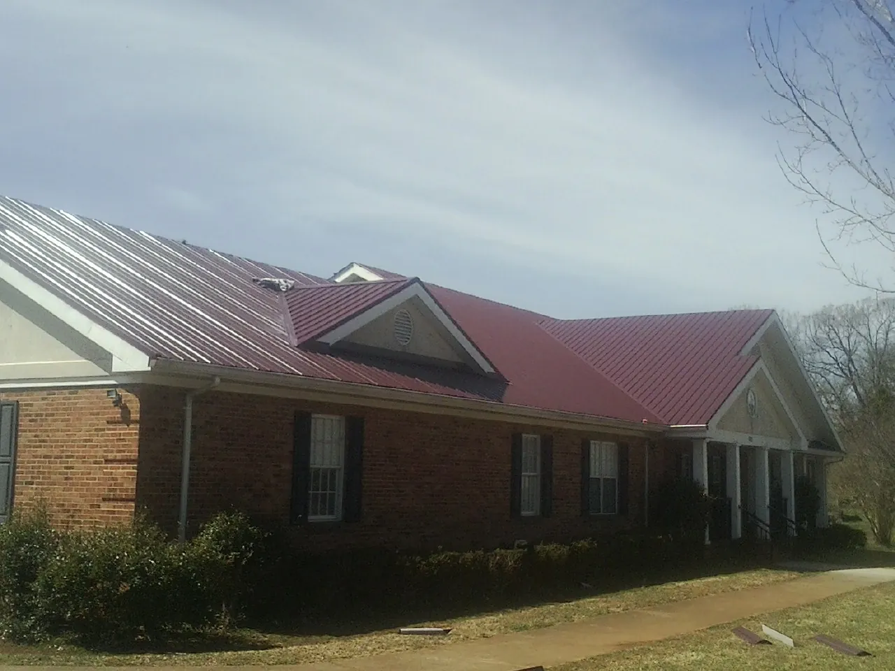 Red metal roof with gabled entries on a long brick building, from a Hail Damage Roof Repair job in Aulander