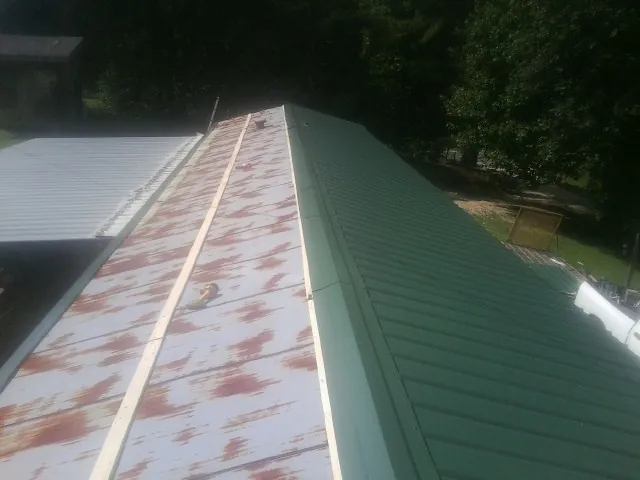 Old rusted panels beside newly installed green metal roofing — Wind Damage Roof Repair by Roofing Brothers in Aulander