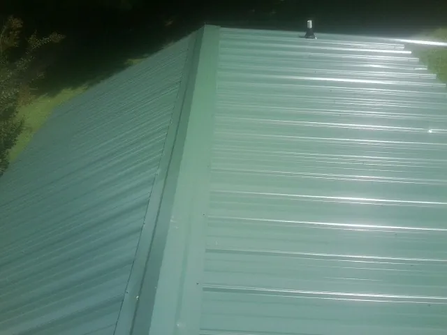 New green metal panels meeting at the ridge of a roof — Flat Roof Repair work by our crew in Aulander